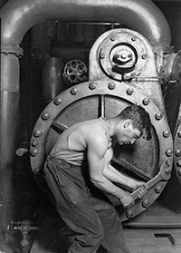 Black and white photo of a man in front of a large metal furnace holding a very large wrench performing heating repair in Ocean County historically