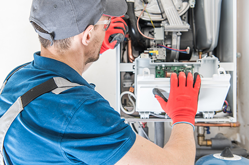 Ocean County furnace repair technician wearing red gloves inspecting an open panel on a furnace